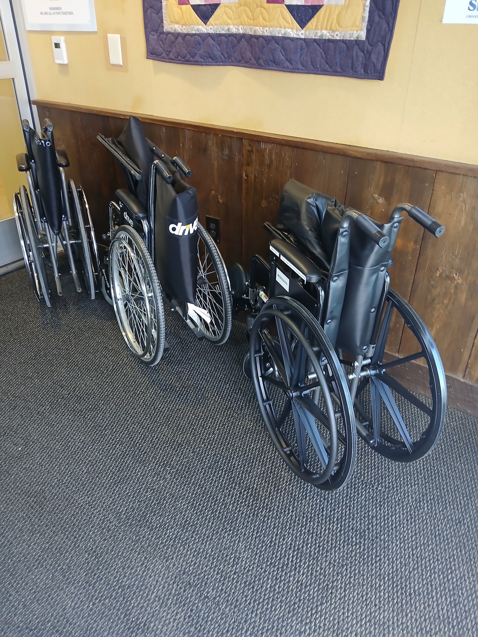 Interior hallway with wheelchairs and mobility aids stored against wood-paneled walls and yellow upper wall sections.