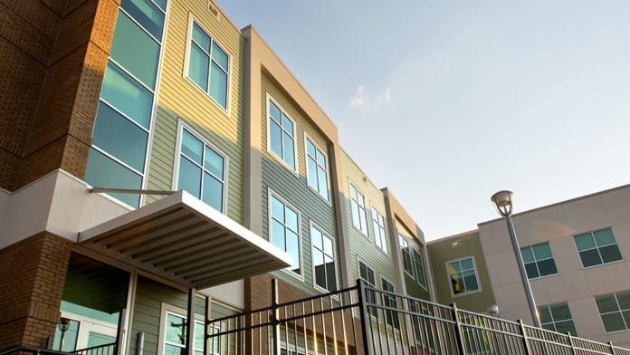 Exterior modern entrance showing brick and yellow metal panel construction, green windows, and metal railings.