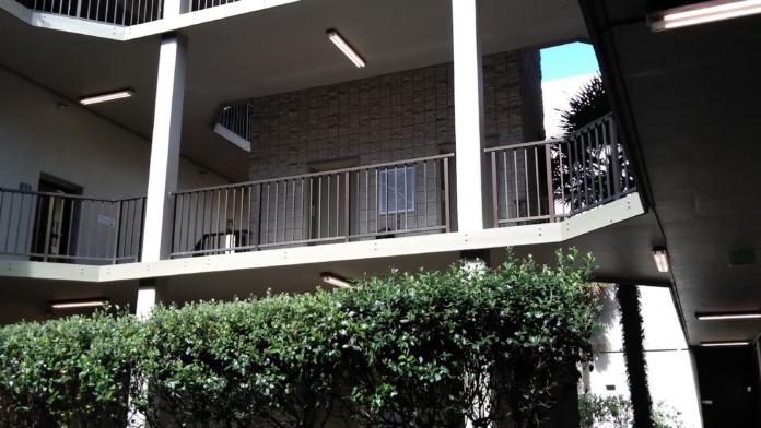 Multi-story exterior showing white railings, balconies, glass panels, and mature landscaping.