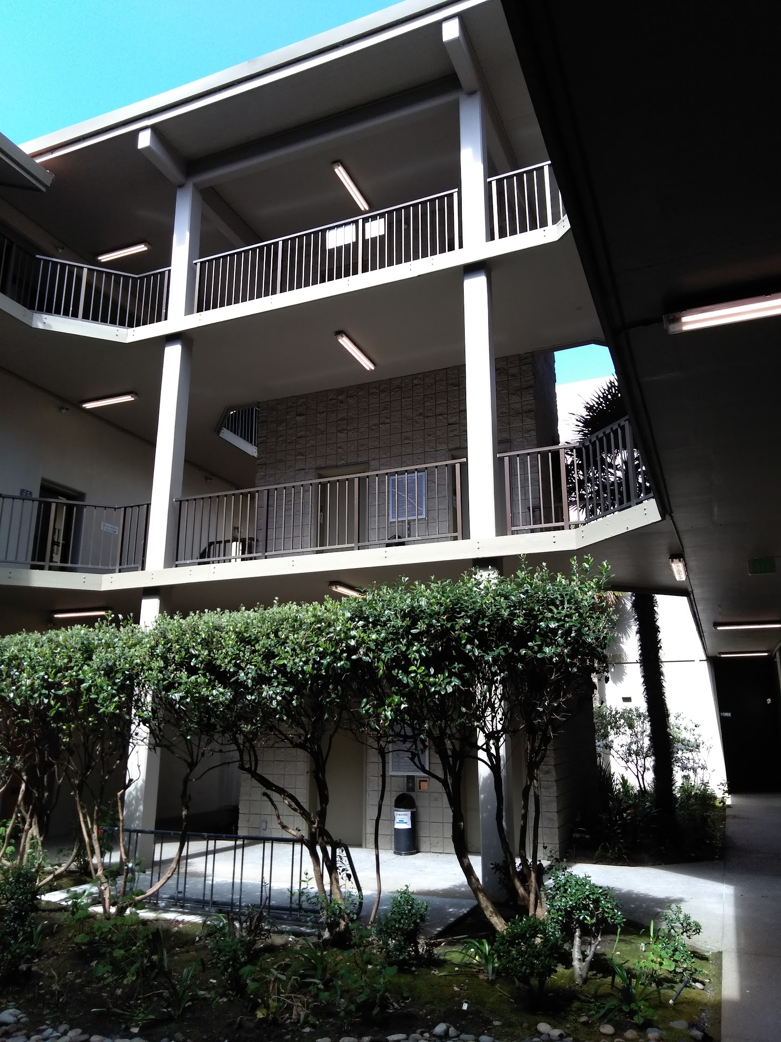 Multi-story exterior showing white railings, balconies, glass panels, and mature landscaping.