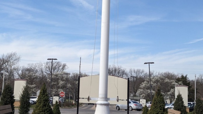 Outdoor grounds with white monument pole, brick walkway, evergreen shrubs, and benches