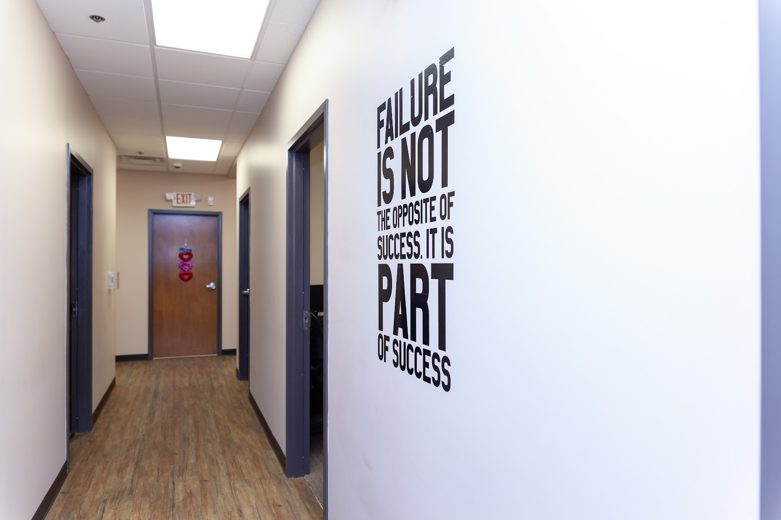 Interior hallway with white walls, dark doors, wood flooring, and motivational text wall decal about success