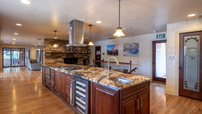 Interior kitchen and living space with wood cabinetry, granite counters, stainless appliances, stone fireplace, and hardwood flooring.