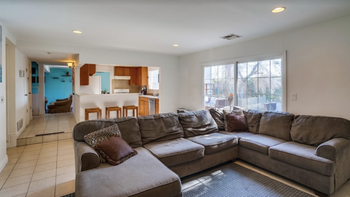 Interior living room with large sectional sofa, sliding glass doors, natural lighting, and kitchen access.