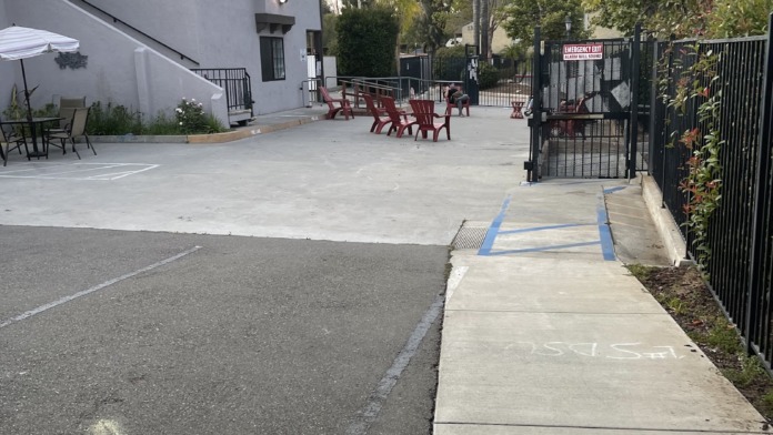 Exterior courtyard with white building, red Adirondack chairs, umbrella, metal gate, and landscaping