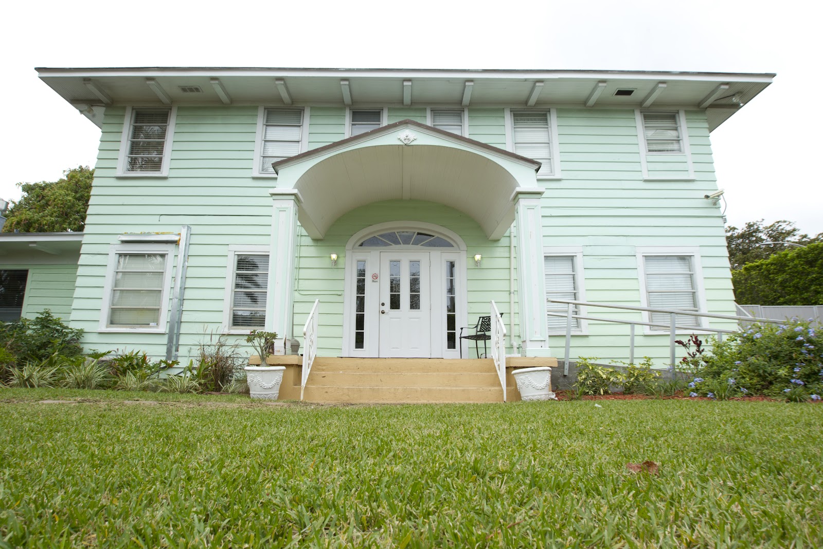 Exterior front facade of two-story pale green house with white trim, arched entrance portico, white doors, windows, and landscaping.