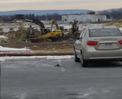 Parking lot area with vehicle and distant view of surrounding facility buildings and terrain.
