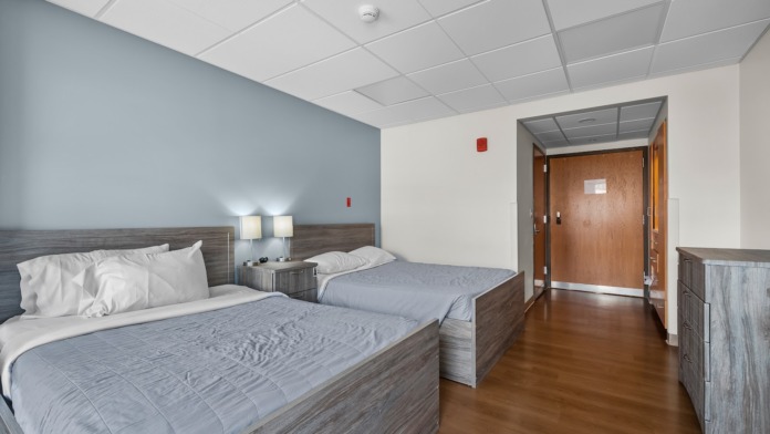 Interior bedroom with two queen beds, blue bedding, wooden headboards, mounted television, and wooden furniture