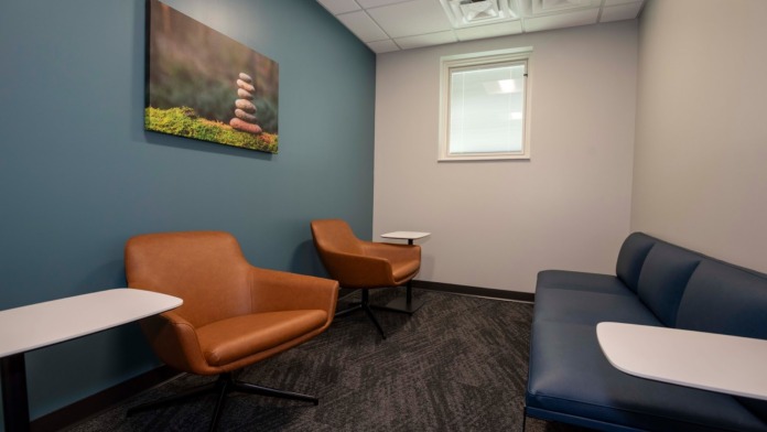 Interior waiting room with teal walls, orange leather seating, navy sofa, and landscape wall art with natural lighting