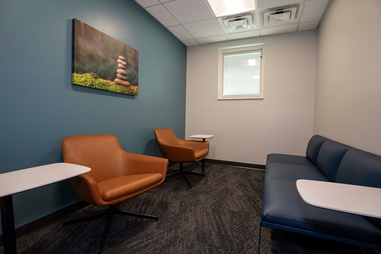 Interior waiting room with teal walls, orange leather seating, navy sofa, and landscape wall art with natural lighting