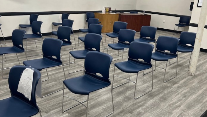 Interior group gathering space with navy blue chairs, wall clock, television, wooden podium, and professional lighting