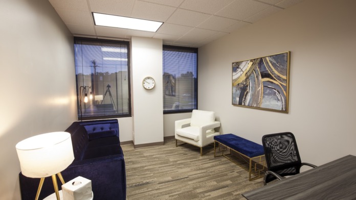 Interior waiting area with white armchair, blue furnishings, illuminated side table, and framed wall art