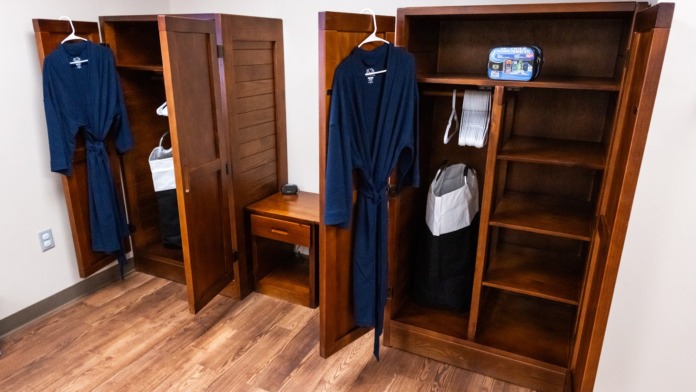 Interior closet space with wooden cabinetry, hanging robes, wooden bench, shelving, and wooden flooring.