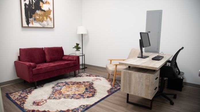 Interior office with burgundy sofa, desk with computer, chair, artwork, and wood flooring