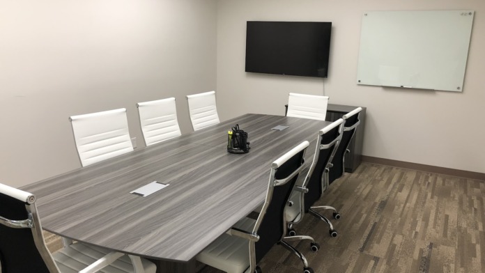 Interior conference room featuring long gray table with white office chairs, mounted television, and whiteboard
