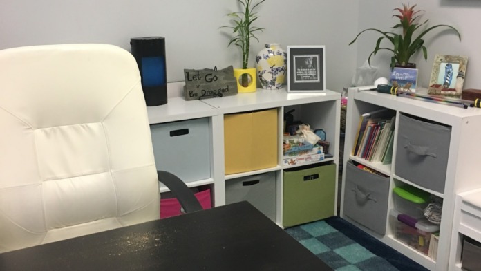 Interior office with white desk, black work surface, colorful storage bins, inspirational wall art, plants, and keyboard.