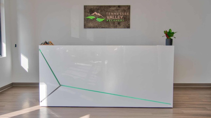 Interior reception area with white desk, facility logo sign, potted plants, and natural lighting