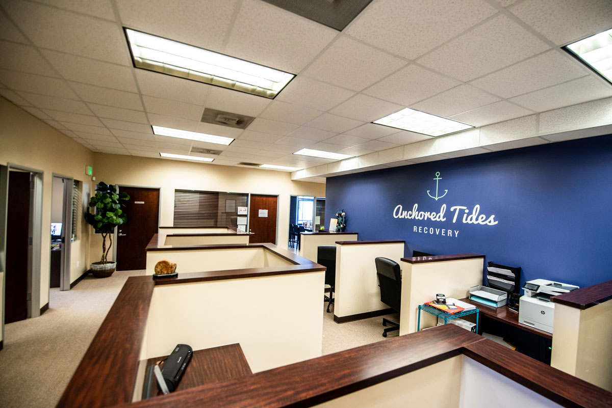 Interior reception desk with blue accent wall displaying Anchored Tides Recovery branding and office workstations