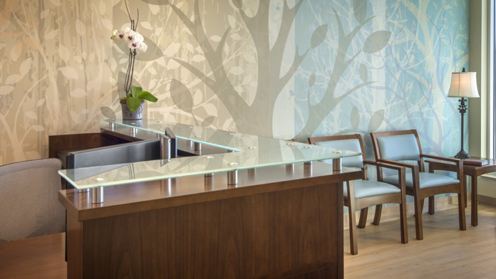 Interior reception area with curved wooden desk, tree-patterned wallpaper, and contemporary furnishings.