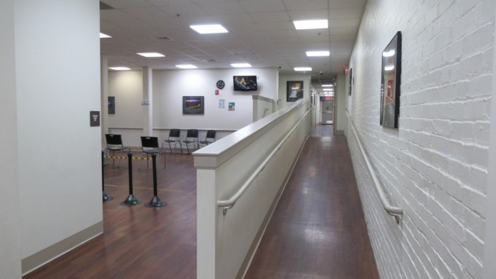 Interior hallway with reception desk, waiting seating, white walls, and dark wood-look flooring