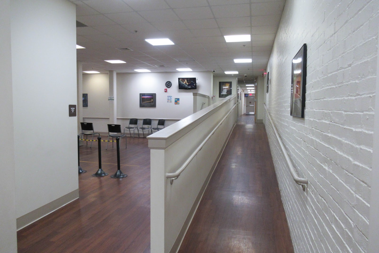 Interior hallway with reception desk, waiting seating, white walls, and dark wood-look flooring