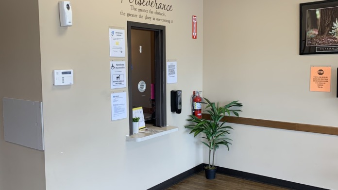 Interior reception counter area with decorative wall text, framed artwork, potted plant, and light wood flooring