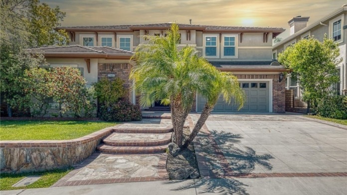 Exterior of two-story brick and stone home with double garage, mature palm tree, and landscaped grounds