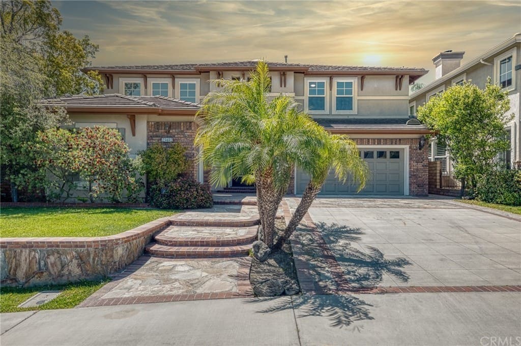 Exterior of two-story brick and stone home with double garage, mature palm tree, and landscaped grounds