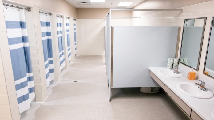 Interior bathroom with multiple shower stalls, striped curtains, white sinks with mirrors, and tiled flooring.