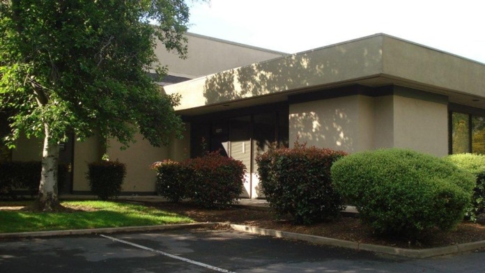 Exterior view of facility building with mature trees, shrubs, and paved grounds