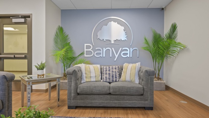 Interior lounge space with gray sofa, decorative pillows, wooden table, plants, and wooden flooring