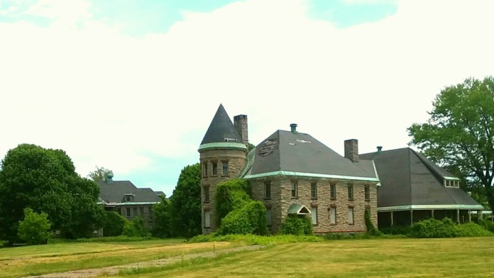 Exterior stone mansion featuring prominent turret and curved entry portico surrounded by mature landscaping