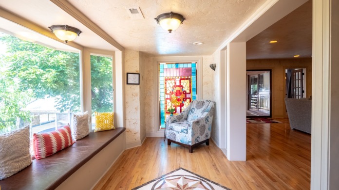 Interior transitional space with large windows, built-in window seat, upholstered chair, and stained glass window detail.