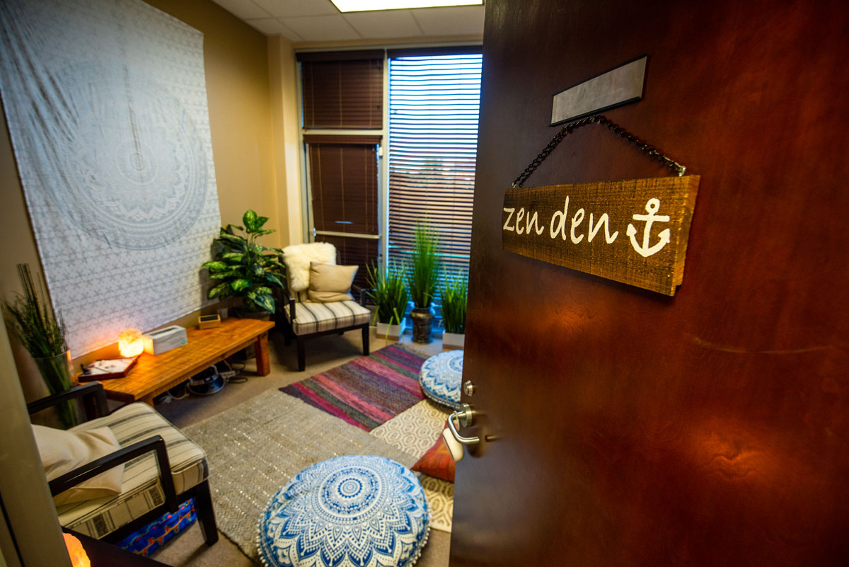 Interior therapy space with comfortable seating, mandala cushions, plants, and wooden anchor wall signage