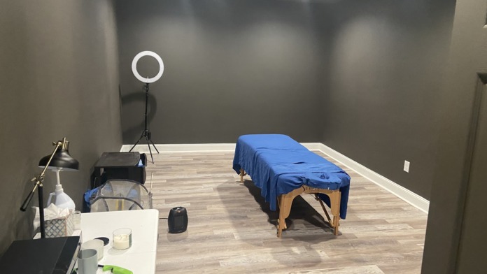 Interior treatment room with massage table, professional lighting equipment, sink area, and modern therapeutic setup