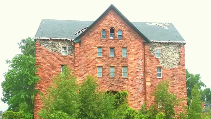Exterior three-story brick institutional building with pitched roof, regular window placement, and surrounding vegetation
