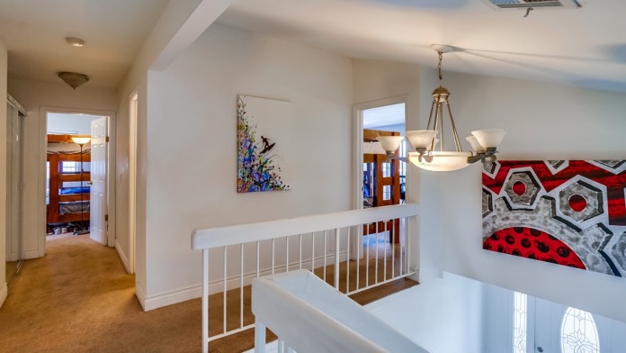 Interior upstairs hallway with white railings, pendant lighting, artwork, and bedroom doorways.
