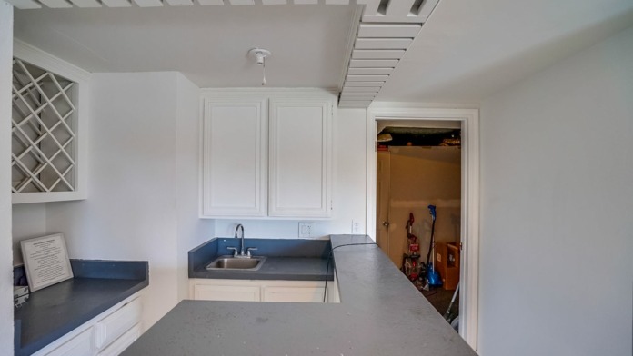 Interior utility room with white cabinetry, blue sink counter, shelving, and adjacent doorway.