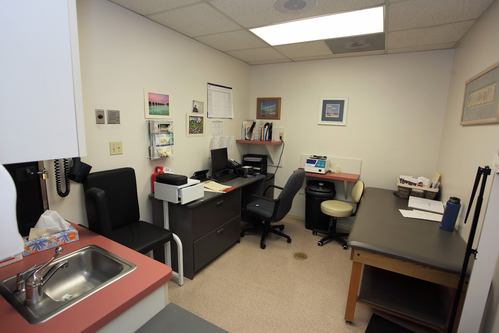Interior administrative office with desks, computer monitors, office chairs, sink counter, and framed wall decorations
