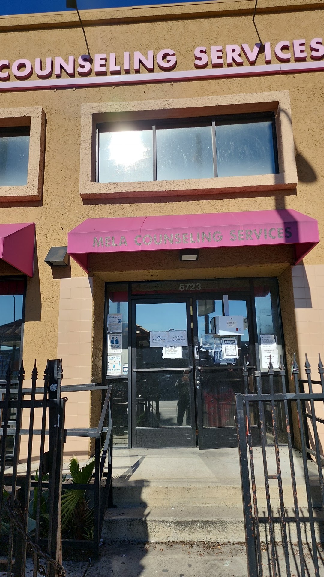 Exterior entrance view showing Mela Counseling Services pink awning, address 5723, and facility logo on cream-colored facade
