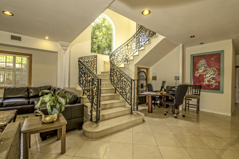 Interior two-story foyer with decorative staircase, ornate wrought-iron railing, sofa seating, artwork, and natural light from windows