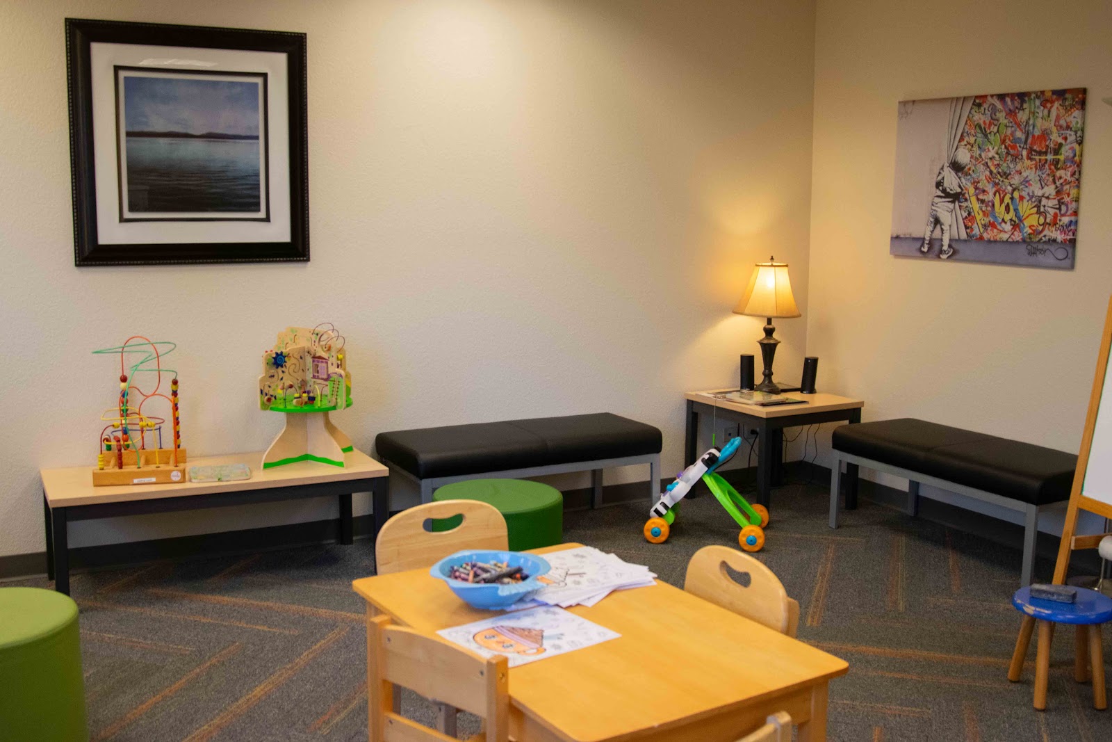 Interior children's play room with activity tables, toys, wall art, seating benches, and soft lighting