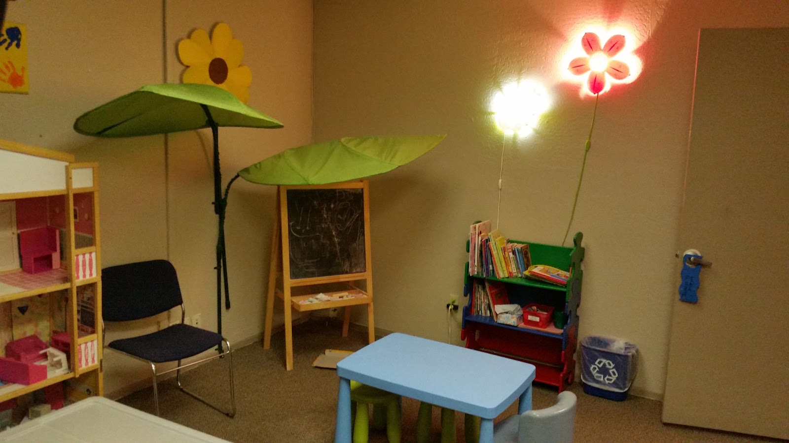 Interior play area with colorful decorative flowers, blue activity table, toy storage, and neon wall decorations.