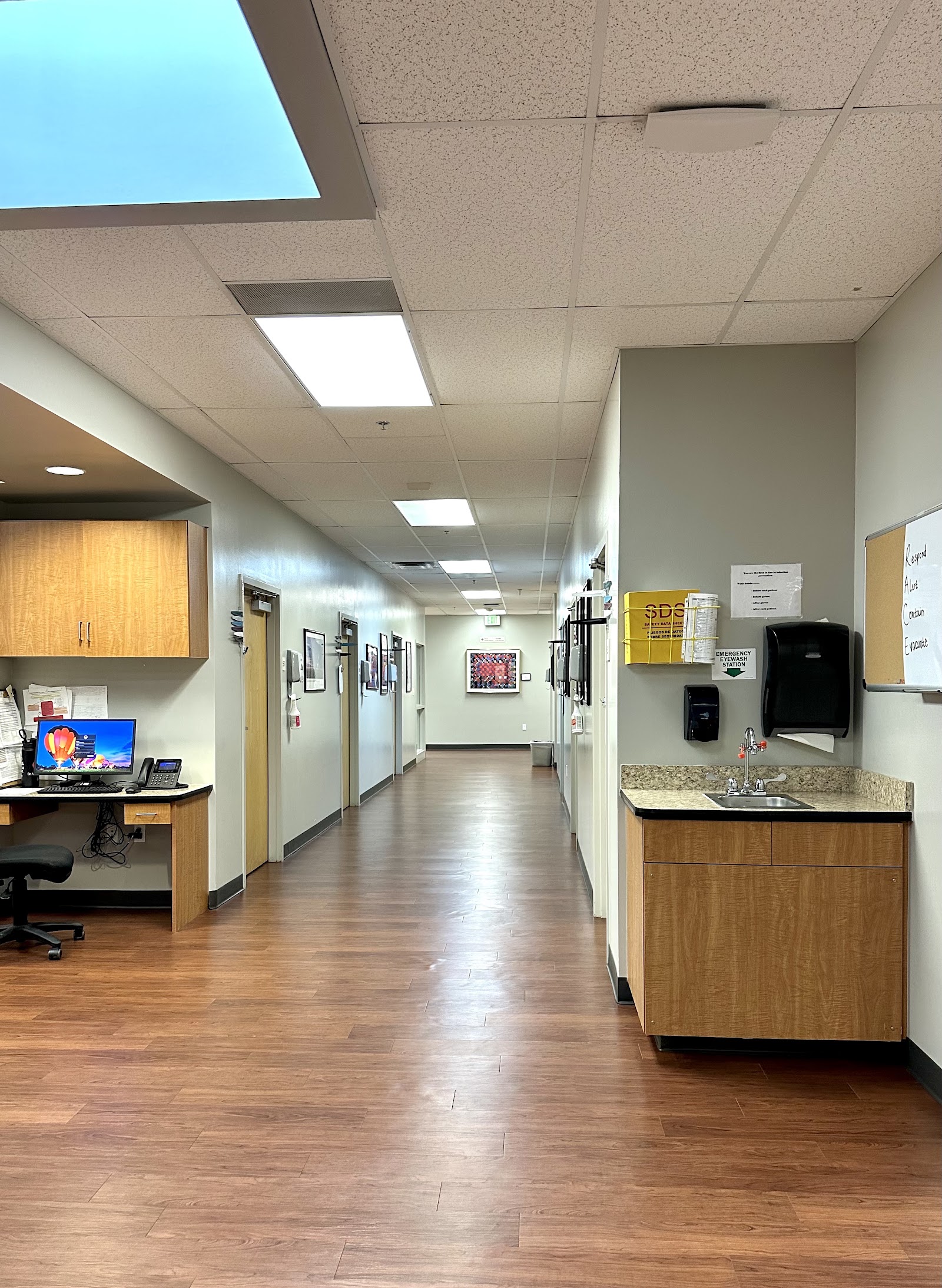 Interior hallway corridor with skylight, office door, sink area, wood flooring, ceiling lights, and posted informational materials