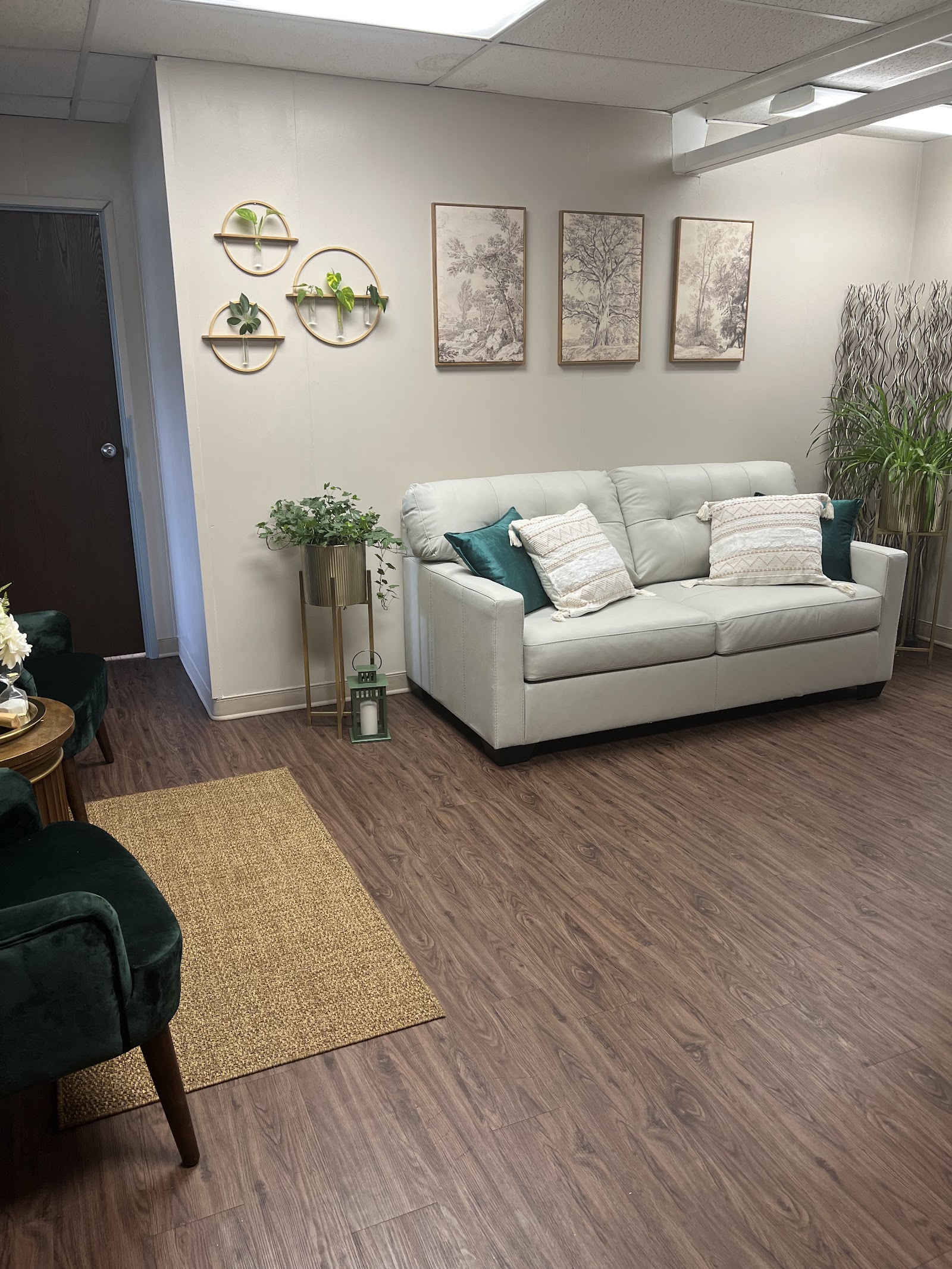 Interior common area with beige sofa, green accent chairs, wall-mounted plants, and decorative tree artwork