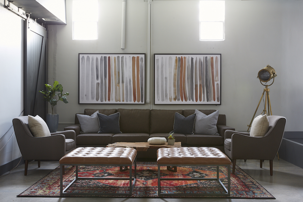 Interior lounge with brown sectional, accent armchairs, potted plant, and framed abstract artwork