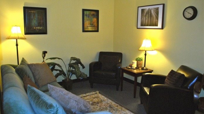 Interior therapy room with comfortable seating, framed artwork, table lamps, and warm yellow walls providing a welcoming environment