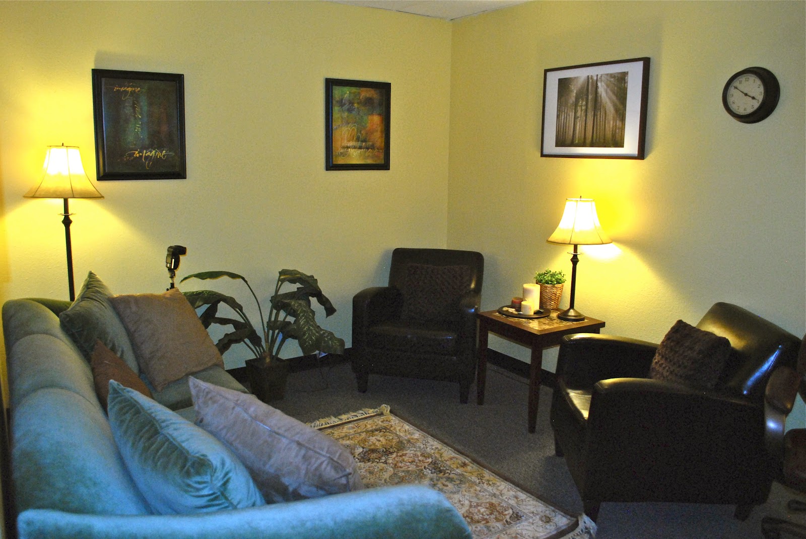 Interior therapy room with comfortable seating, framed artwork, table lamps, and warm yellow walls providing a welcoming environment