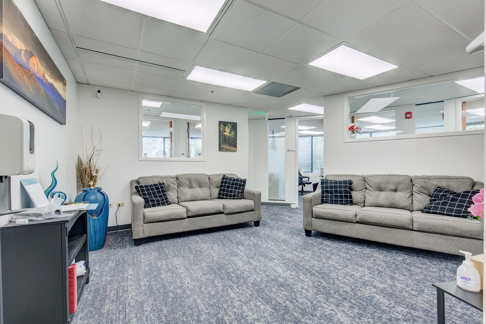 Interior common area with two beige sofas, decorative pillows, side tables, wall art, and bright ceiling lighting