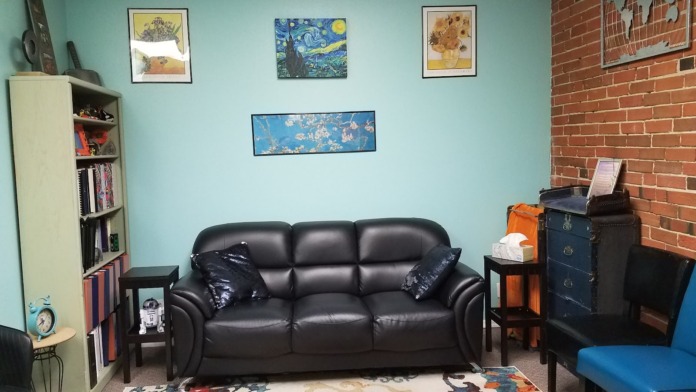 Interior common room with turquoise walls, black leather sofa, bookshelf with books, art prints, and exposed brick accent wall